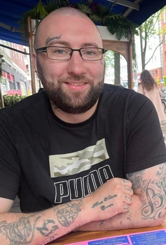 34-year-old white man with cropped dark hair and beard. Wearing glasses and a black t-shirt