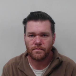 Image of jailed man George McDonald - Middle aged man with dark hair with ginger beard wearing brown zipped jumper with white tshirt underneath