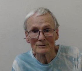 79-year-old white man with grey hair and wearing glasses. Wearing a blue and white t-shirt