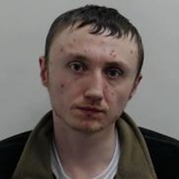 Image of man sentenced John McKechnie - white man with short dark hair and slight stubble and spots on face. Wearing dark-coloured pullover and white tshirt.