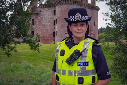 Chief Supt Carol McGuire standing at Drumlanrig Castle. She is wearing full black police uniform and hat with a hi-vis vest holding police equipment.