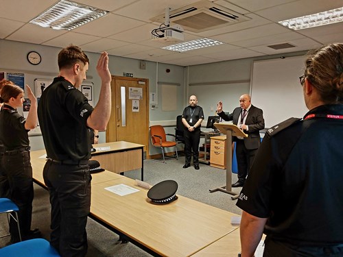 Police Scotland probationary constables dressed in black uniforms raise their right hands to take the Oath of Office in Inverness.