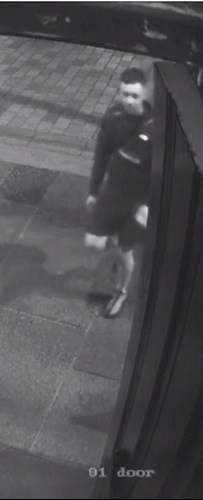 A black and white CCTV image showing a man wearing a dark-coloured top and shorts. He is pictured in the street.