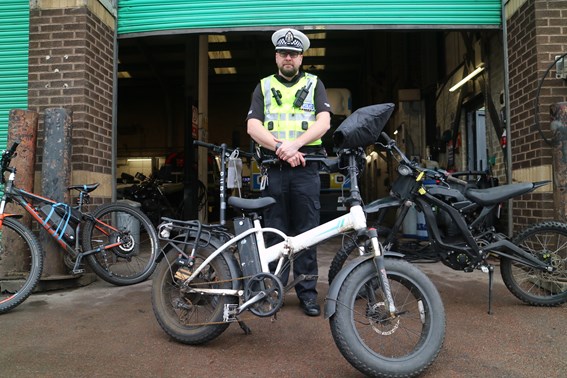 Image of Inspector Hugh Niccolls in high-vis vest, police hat in front of garage with white e-bike