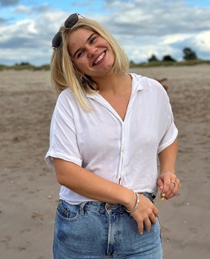 21-year-old woman with blonde hair wearing a white top and jeans smiling