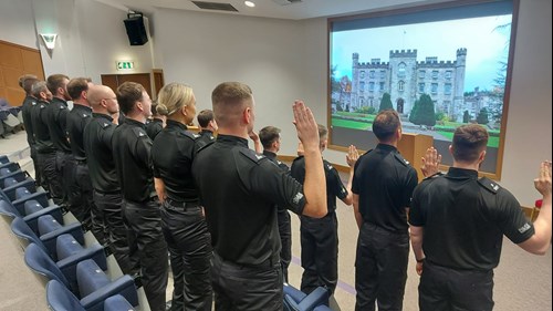 Police Scotland probationary constables dressed in black uniforms raise their right hands to take the Oath of Office in the Tulliallan Lecture Theatre.