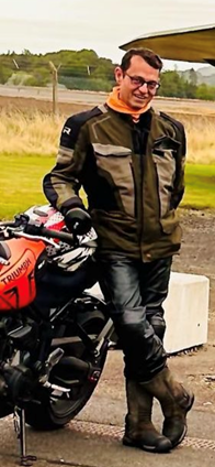 Image of man who died Allan Robertson - middle aged man with dark hair wearing dark-rimmed glasses, dark motorbike clothing next to red motorbike